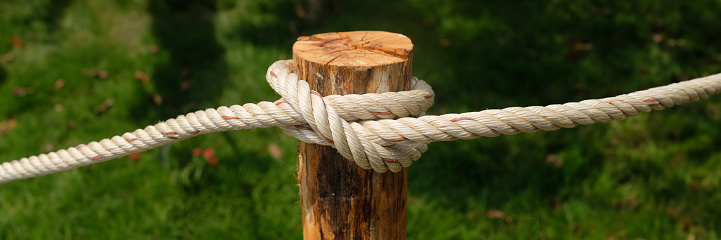 Close up white rope twisted on wooden pole with green bokeh background