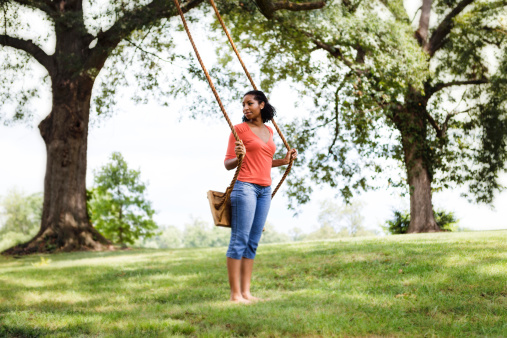A woman in the park with a swing hanging from a tree.  