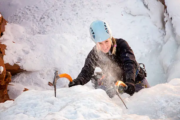 Young woman climbing a frozen waterfall with ice climbing gear