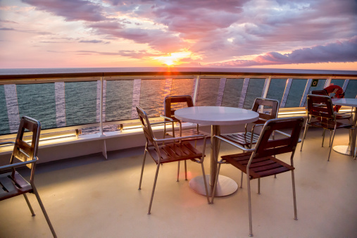 Sunset on a cruise ship with tables and chairs.  Carefully shot scene making sure that no copyrighted ship design is depicted.
