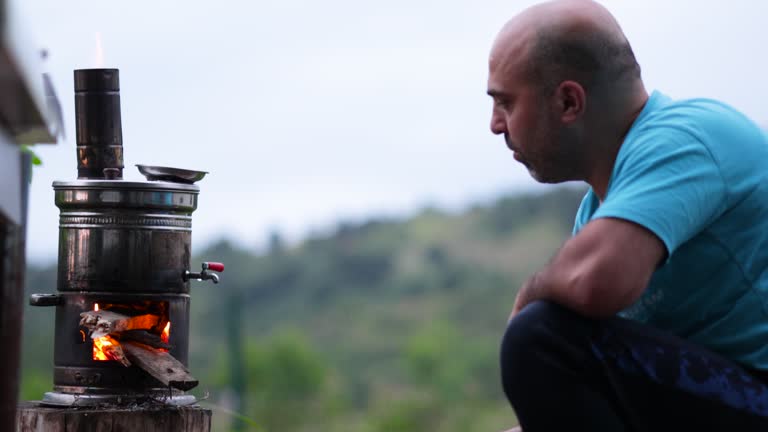 A man stoking the flames of the samovar and adding firewood to the samovar