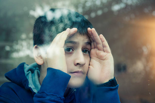 istock A young boy peers through a clear glass window  168627450