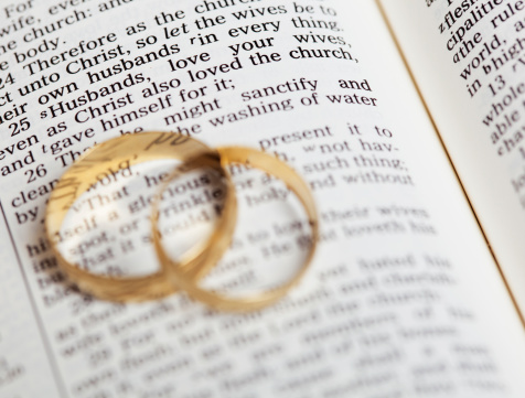Gold wedding bands placed on a King James Version Bible. The passage is Ephesians 5 