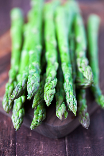 Fresh stalks of asparagus on a wood cutting board and a wood table.