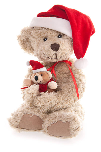A teddy bear is sitting on a red ribbon with a Christmas tree on its chest. The bear is wearing a hat and scarf, giving it a festive and cozy appearance
