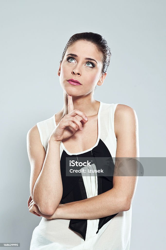 Thinking young woman, Studio Portrait Portrait of attractive young woman looking up with index finger on chin. Studio shot on a grey background. Women Stock Photo