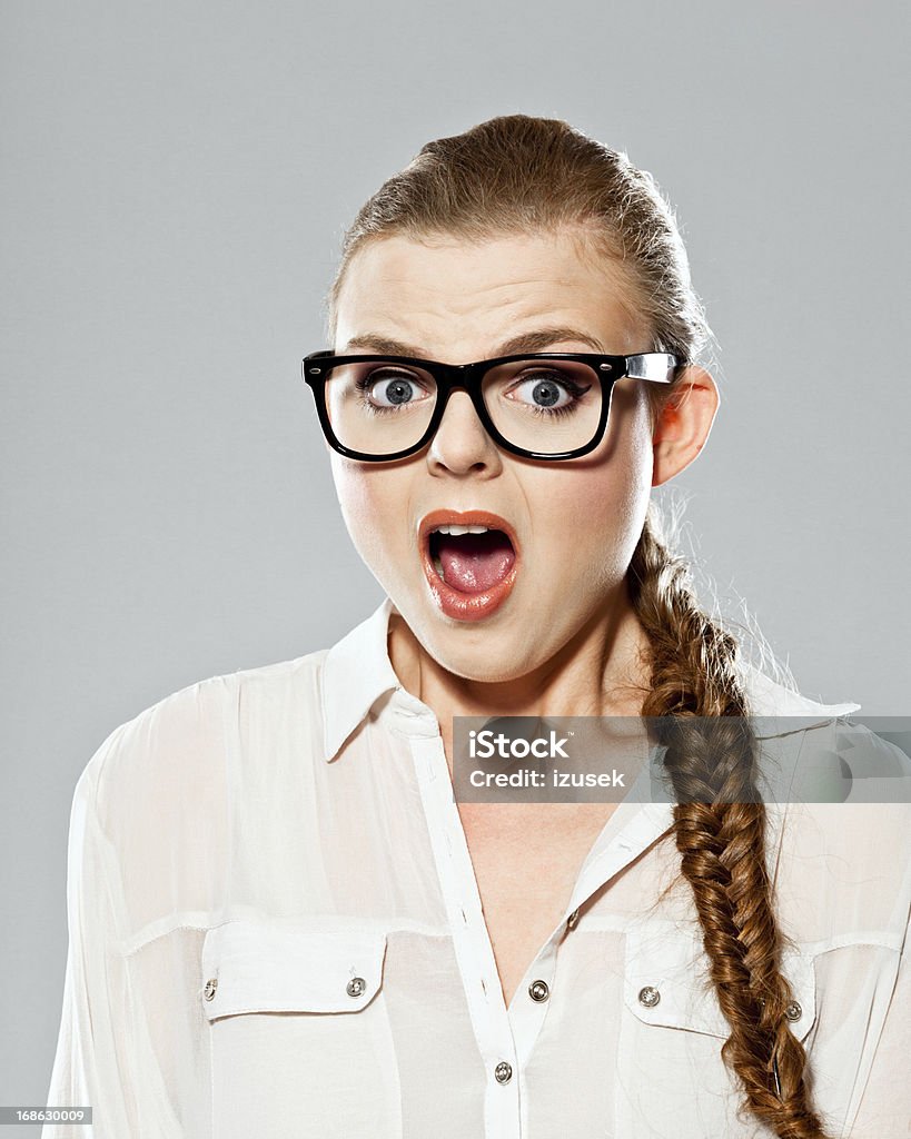 Deadline Portrait of frightened young adult woman wearing nerd glasses staring at camera with mouth open. Studio shot on grey background. Human Face Stock Photo