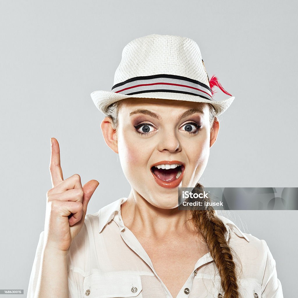 Idea Portrait of excited young adult woman pointing with index finger at copy space, looking at camera with mouth open. Studio shot on grey background. Index Finger Stock Photo