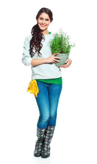 Full lenght portrait of beautiful gardener holding a rosemary in hands and smiling at the camera.