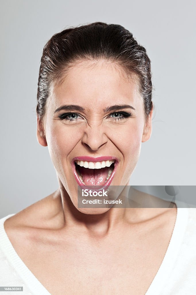 Young woman screaming, Studio Portrait Portrait of young woman screaming at the camera. Studio shot on a grey background. Mouth Open Stock Photo