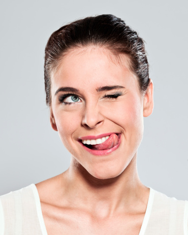 Portrait of attractive young woman sticking out her toungue and squinting. Studio shot on a grey background.