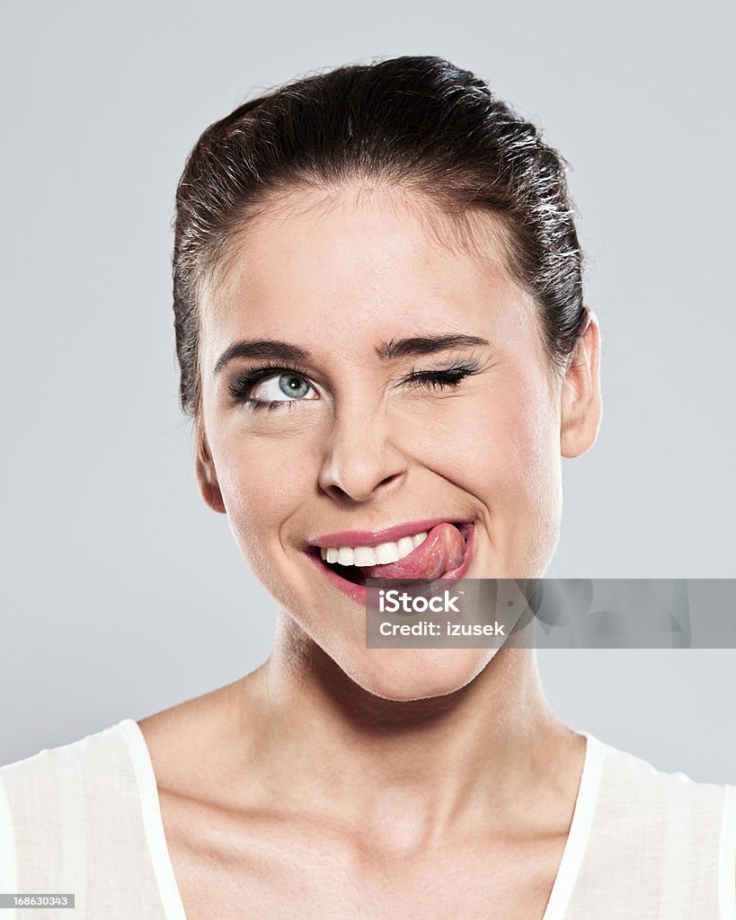 Attractive young woman grimacing Portrait of attractive young woman sticking out her toungue and squinting. Studio shot on a grey background. Women Stock Photo