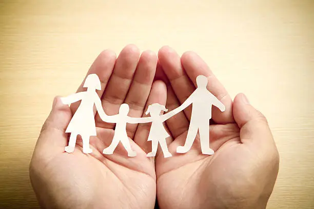 Photo of Paper family in hands with wooden texture background