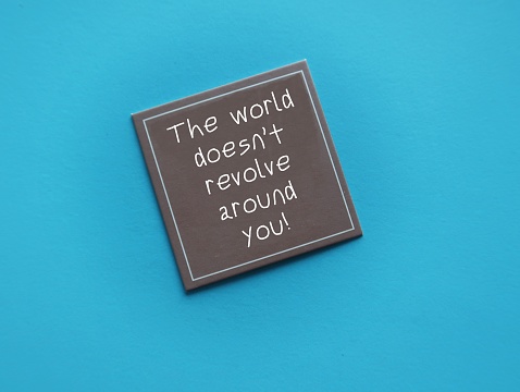 Brown card on blue background with handwritten text- The world doesnt revolve around you - to remind we are the center of the universe, not as important that much, stop taking everything personally