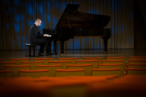 Mid adult man playing the grand piano while performing piano concert in a concert hall.