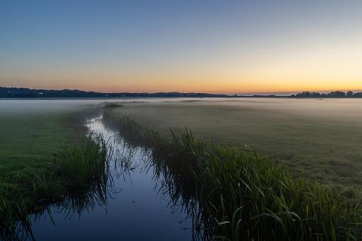 After a warm summer day, the sun slowly sets, and low-lying mist forms above the meadows along the coast of North Holland in the Netherlands.