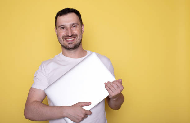 istock Smiling handsome young bearded man holding underarm laptop pc computer isolated on yellow background. 1686350698