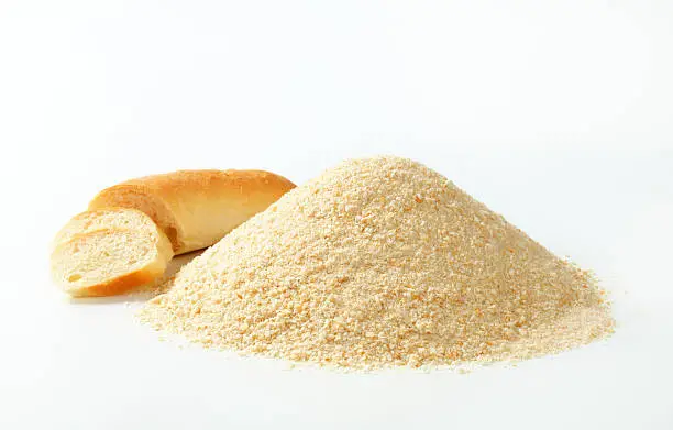 fresh breadcrumbs heap and a sliced hard roll on a white background