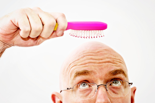 A nearly bald man looks up, eyebrows raised, as he eyes his last hair in the pink hairbrush he holds. Brushing  is an exercise in futility! 