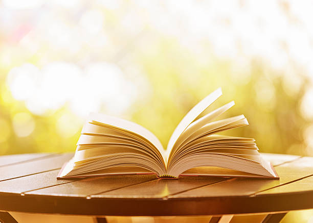 abrir libro de tapa dura descansar en mesa de jardín en la suave luz del sol - outdoors book reading accessibility fotografías e imágenes de stock