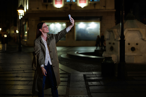 Seeking connection and engagement, a woman delves into the digital universe through her mobile phone on a nighttime city adventure, finding solace and inspiration in the virtual spaces that coexist alongside the bustling urban streets