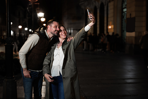 Sharing a digital adventure, a couple engages with their mobile phones on the city street, their laughter and conversation intermingling with the urban ambiance, as they navigate the virtual landscape together, deepening their connection and building memories