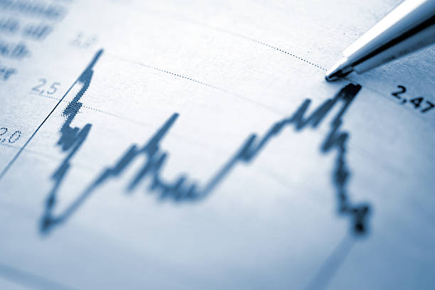 Finance chart with high peak on document image of a macro shot from a chart with high peak on newspaper and a silver pen, blue toned image progress report stock pictures, royalty-free photos & images