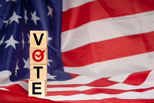 Side view of wooden cubes with letters VOTE on the American flag background. United States presidential election. Politics and voting conceptual