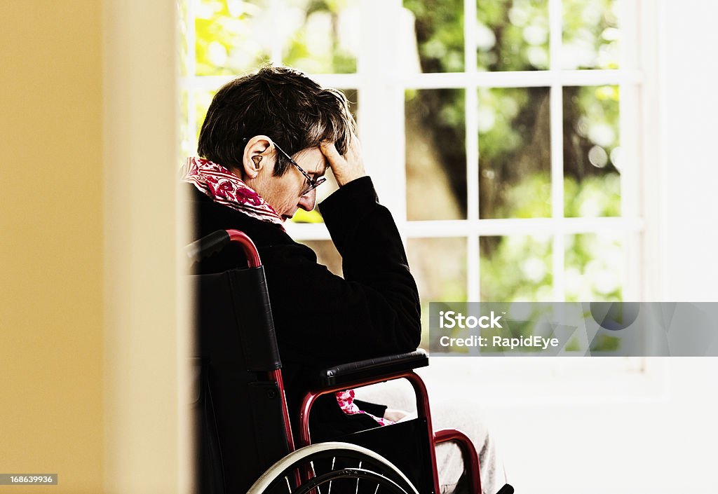 Old mulher em cadeira de rodas, com cabeça nas mãos, é pressionado - Foto de stock de 70 anos royalty-free