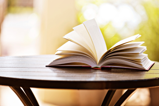 A hardback book lies open on a table against a soft-focus garden background. A reminder that a good old-fashioned book can provide you with portable education, entertainment, inspiration or just good company!