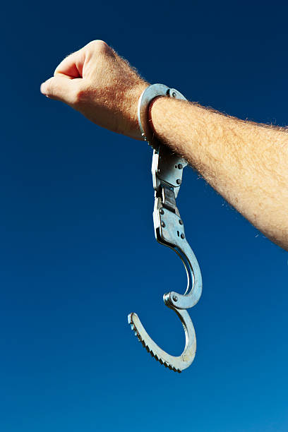 Free at last! Hand with clenched fist and open handcuff A man's hand, holding up a clenched fist in a salute, and wearing a single, open handcuff, is brandished against clear blue sky. Symbolic of release or freedom from almost anything!  bail stock pictures, royalty-free photos & images