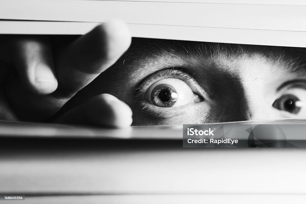 AMPLIA-eyed Aterrorizado hombre peeping aunque persianas venecianas - Foto de stock de Echar un vistazo libre de derechos