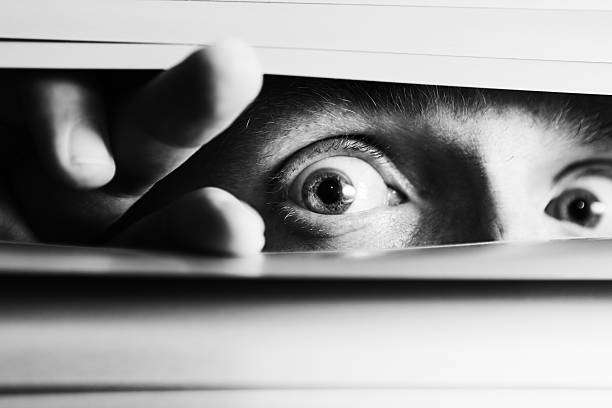 Wide-eyed terrified man peeping though venetian blinds
