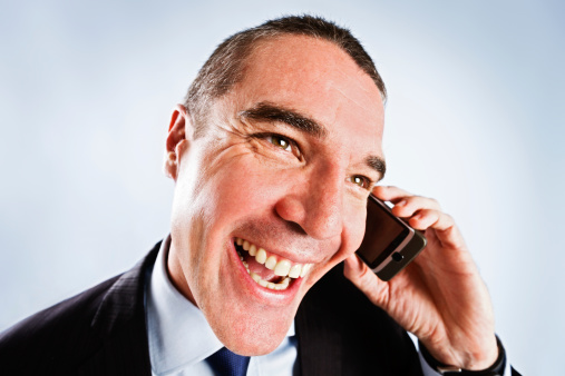 Distorted head and shoulders shot of a businessman listening to something on his mobile phone and looking almost too delighted at what he hears. Could be a persistent door-to-door salesman or an unwanted caller, seen through a peephole.