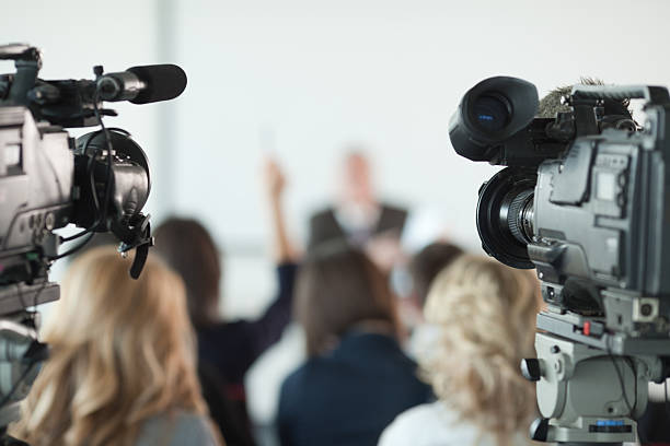 Press conference. Video cameras pointed at businessman or lecturer giving a presentation in background. Focus on cameras.   press room photos stock pictures, royalty-free photos & images