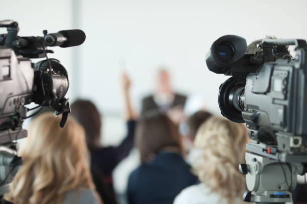 Press conference. Video cameras pointed at businessman or lecturer giving a presentation in background. Focus on cameras.   press conference stock pictures, royalty-free photos & images