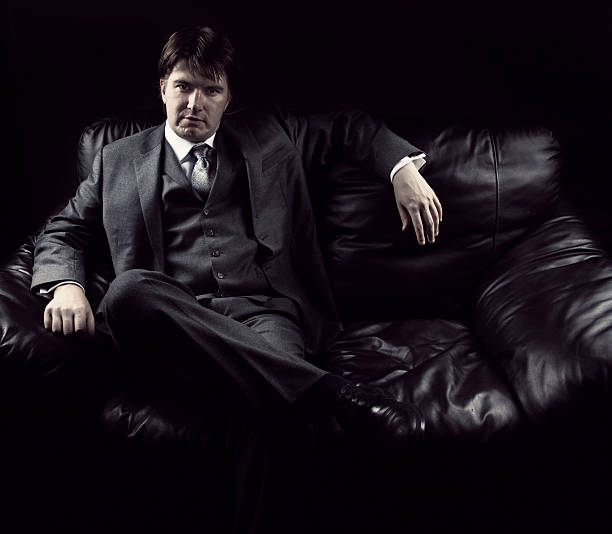 Young man sitting on the couch Dark portrait of young man sitting on leather brown couch mafia boss stock pictures, royalty-free photos & images