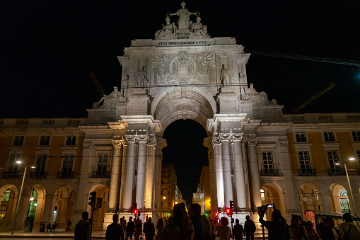 Lisbon, Portugal - October 09 2022: Famous Augusta Arch at night, illuminated. Situated in the city center of Lisbon, Portugal. Street lights on. Travel destination. Night photography. People passing