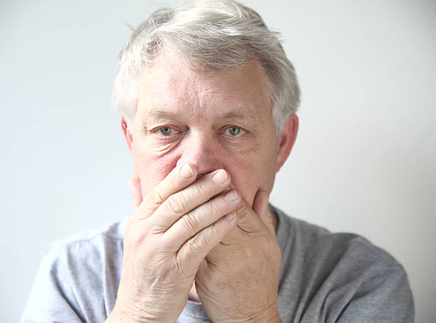 senior man holds his hands over his mouth