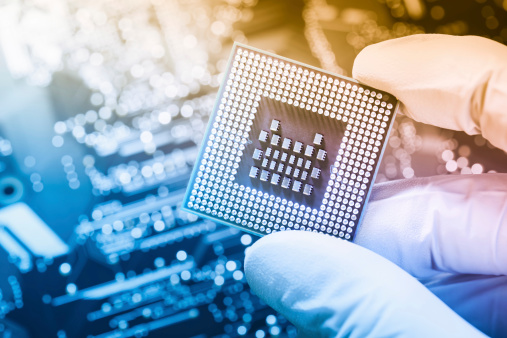 Electronic technician with glowes holding chip. Nice bokeh from circuit board in background. Warm light from top right corner. 