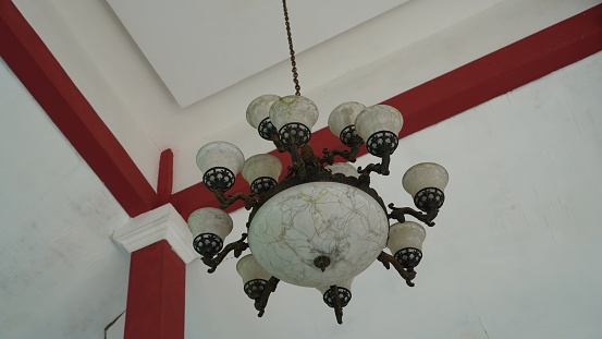 an ancient chandelier in the middle of the room with a red pillar background