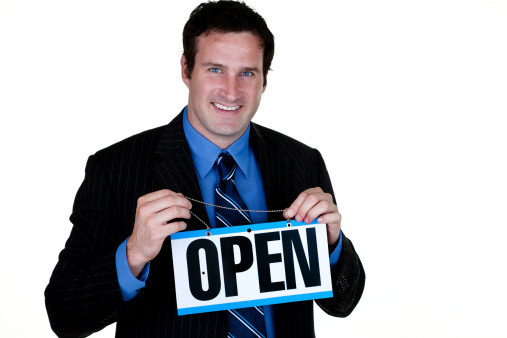 Cheerful man in his 30s wearing a suit and holding an open sign while being isolated on white background 
