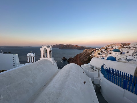 View through an open window with shutters of the whitewashed village of Oia rising above the blue Aegean Sea and the caldera on the island of Santorini, Greece.