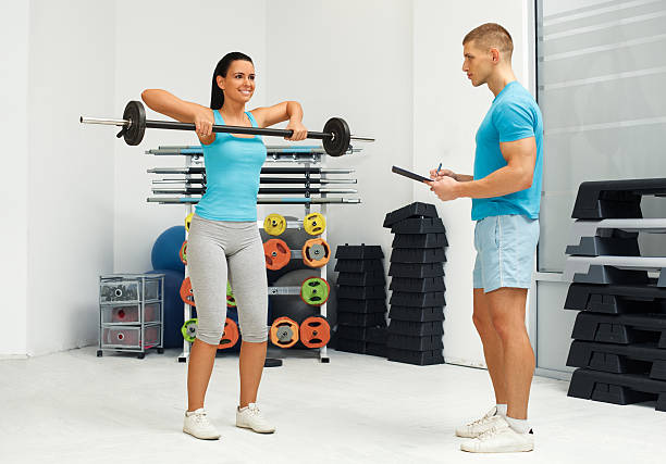 Personal male trainer watching young woman who lifting barbells