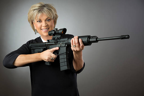 ältere frau hält ein gewehr auf grauem hintergrund. - gun women handgun armed forces stock-fotos und bilder