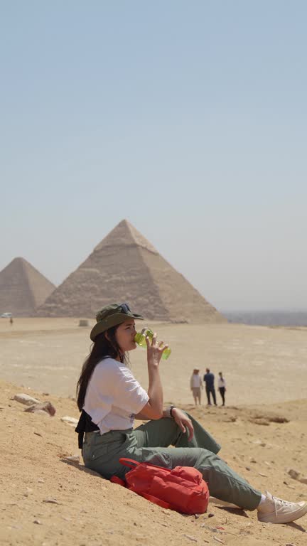 Egypt, Cairo, asian woman tourist sitting  on rocks with Great Pyramid of Giza in background