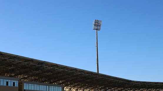 fragment of a stadium with part of the roof, covered spectator stands and a lighting spotlight on a high mast, elements of the architectural composition of a sports arena with lighting equipment