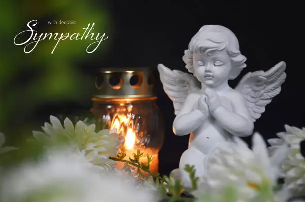 Photo of Sympathy card with an angel, votive candle and flowers on black background