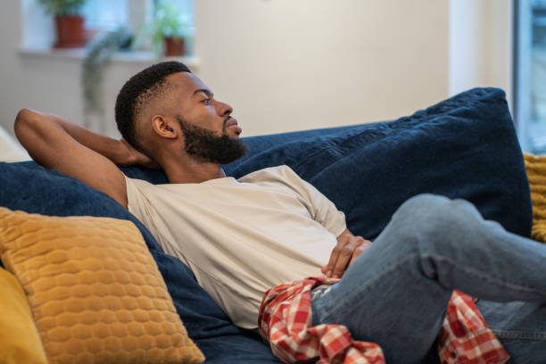 istock Thoughtful dreaming african american guy sits on sofa rests in studio apartment. 1686605878