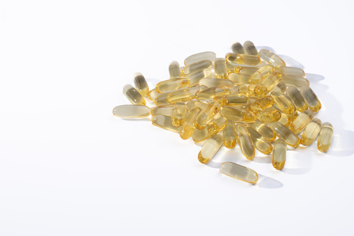 Pile of golden, fish oil softgels on a white background.